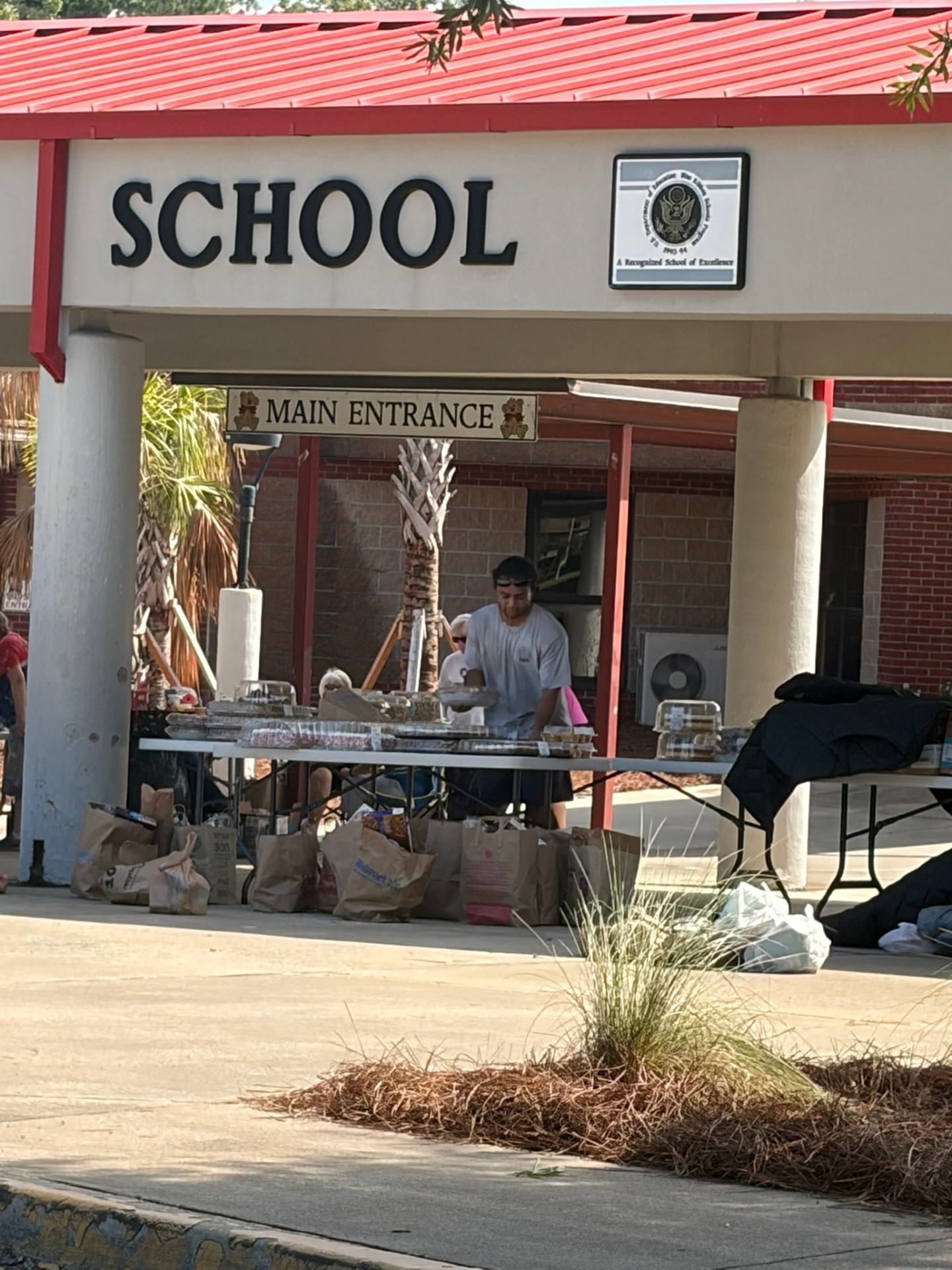 Tables and bags of donated food prepared outside a school entrance.