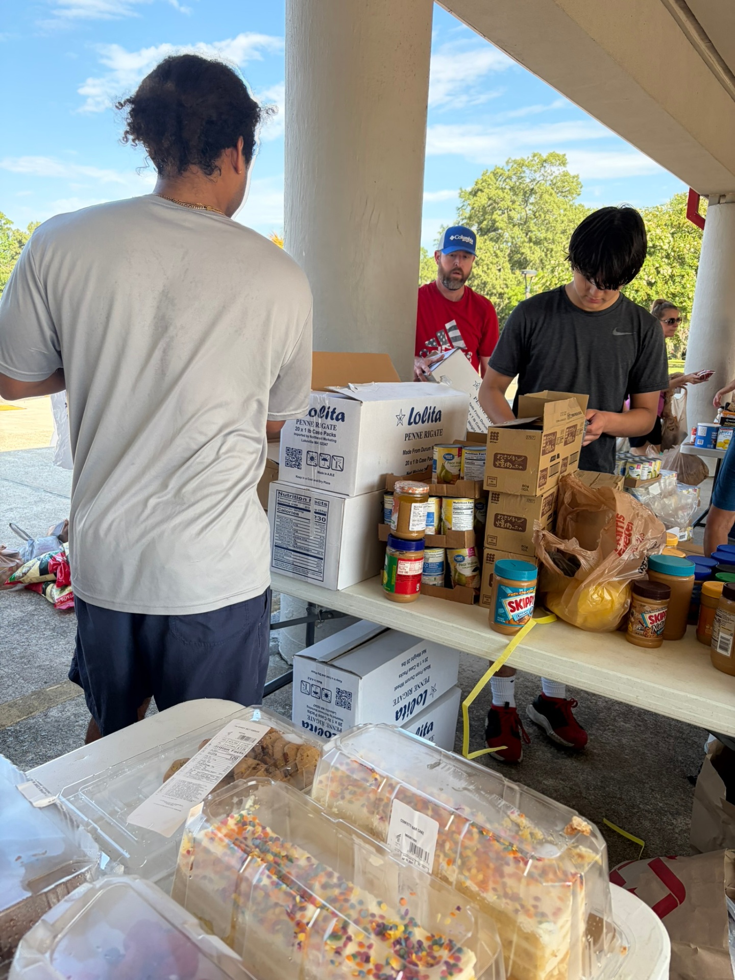 Volunteers sorting packaged food and donated supplies on tables.