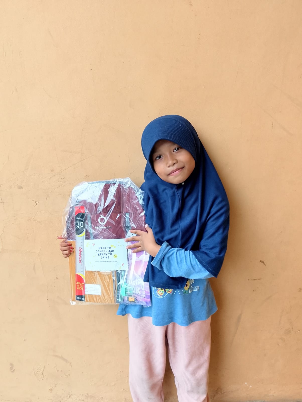A student holding a wrapped back-to-school kit with notebooks, a ruler, and stationery.