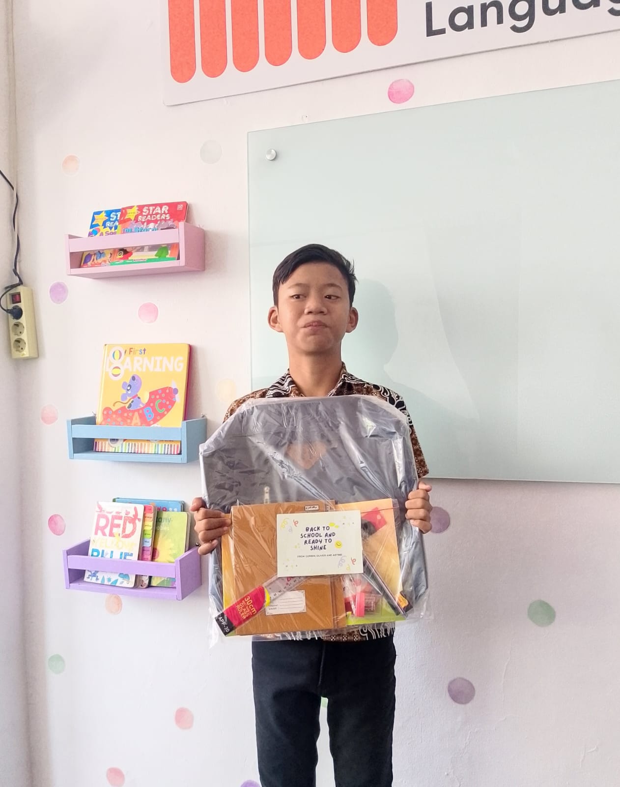 A student holding a back-to-school supply kit with notebooks and stationery.