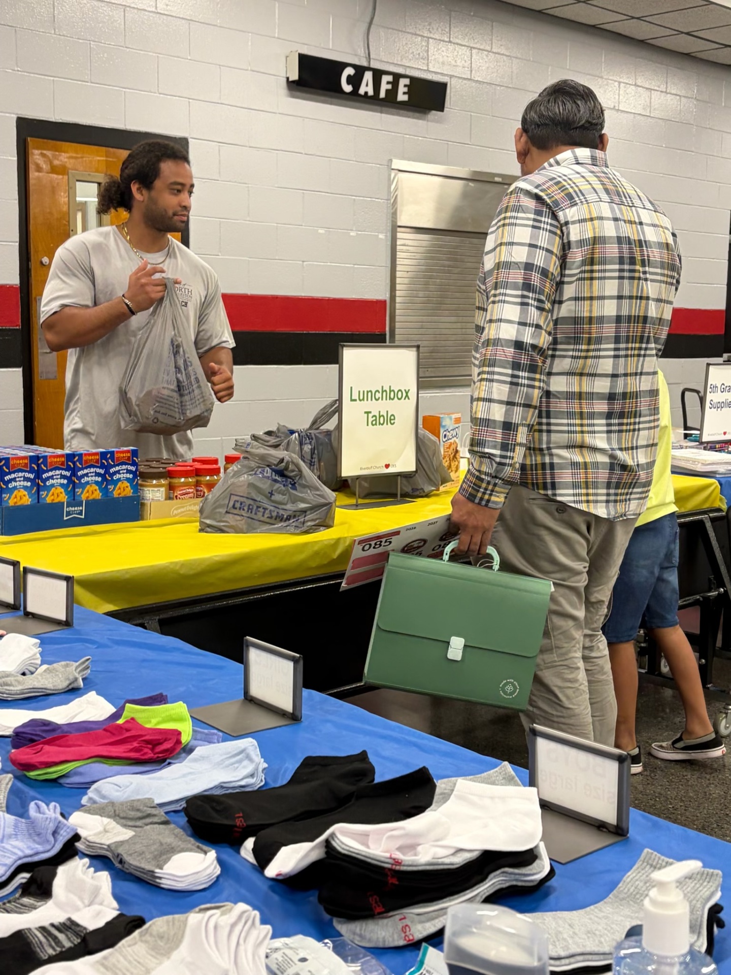 A volunteer assisting an attendee at a table with socks, toiletries, and family supplies.